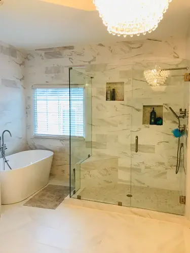 Freestanding bathtub and frameless glass shower in a modern bathroom with marble tile walls