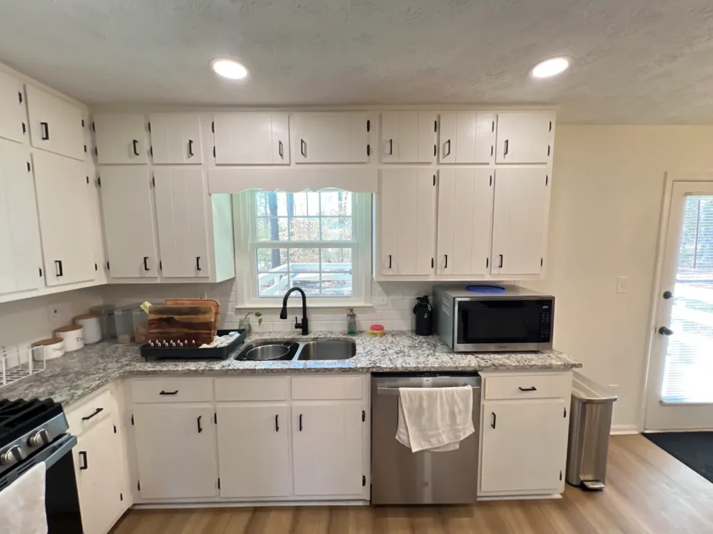 Kitchen with white upper and lower cabinets, granite counters, and a central window over the sink