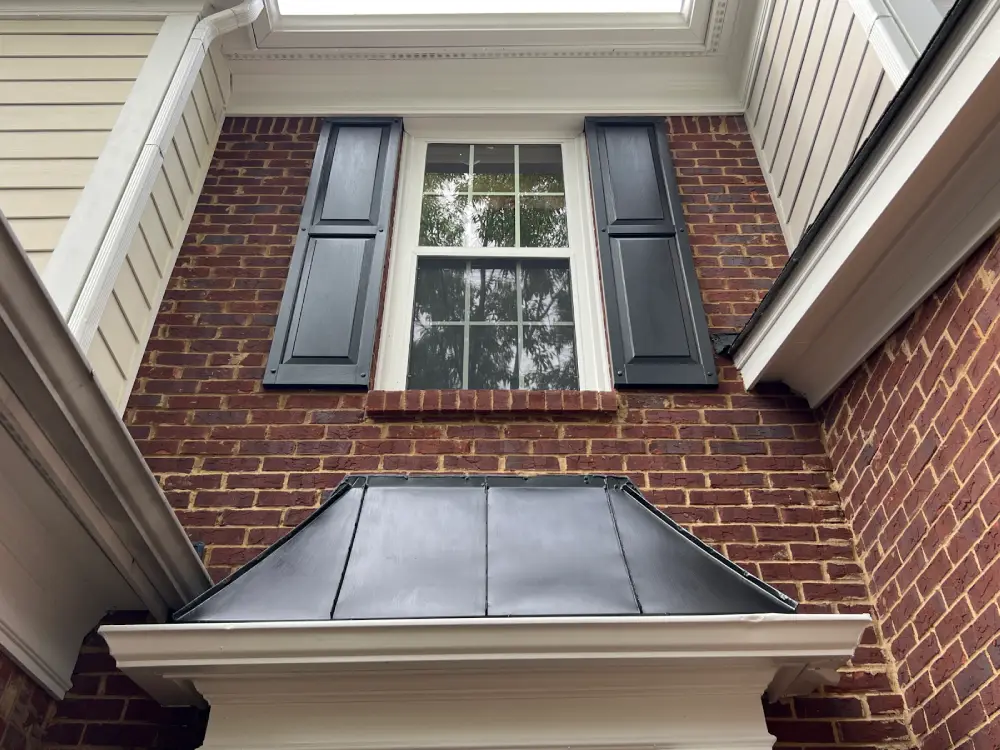 A brick building in Monroe featuring a window and a metal roof against a clear sky